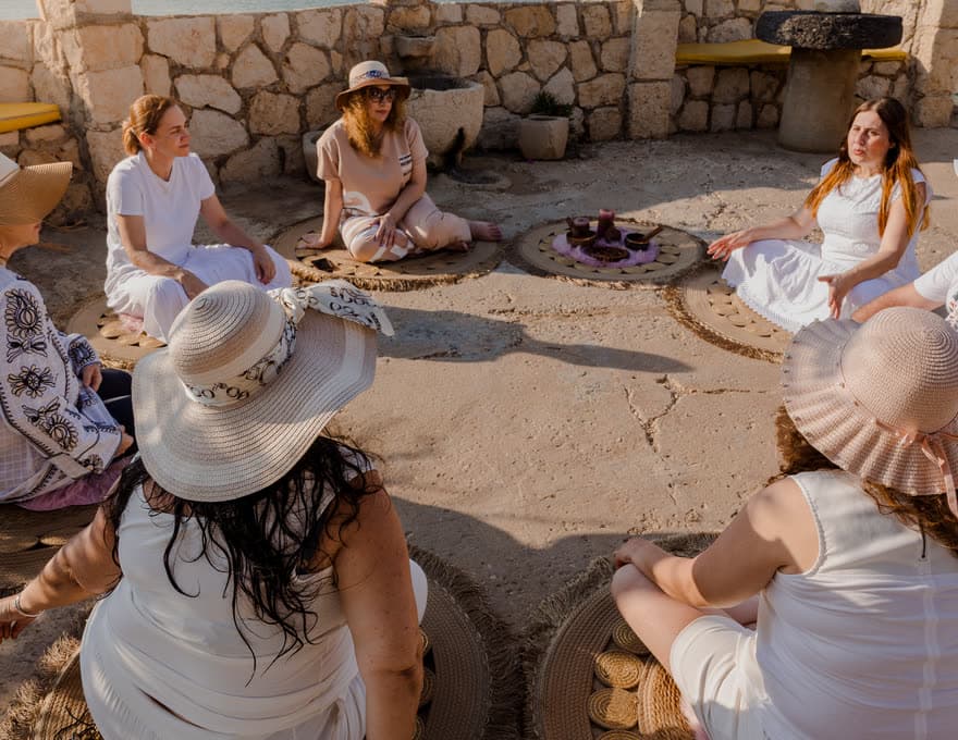 A circle of retreat participants seated on woven mats around a small altar on a seaside terrace in Lebanon
